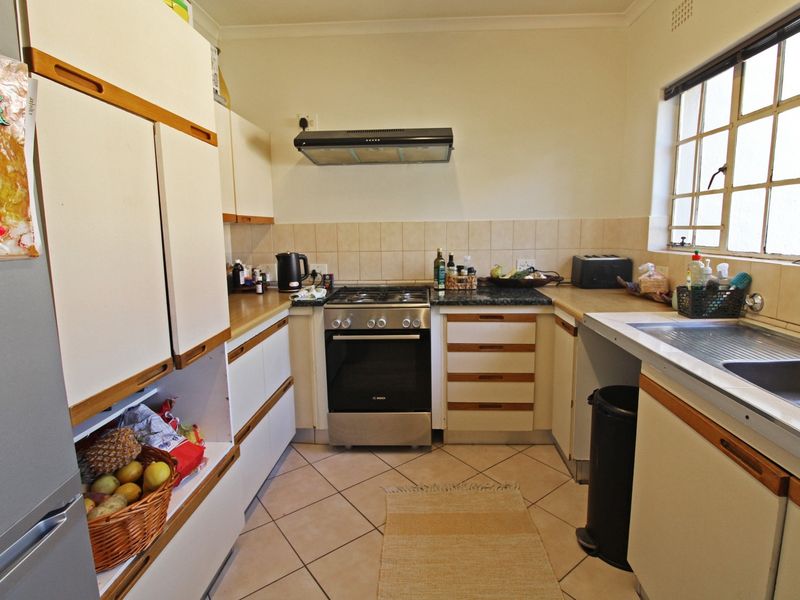 A functional kitchen featuring built-in cabinetry, a gas stove with extractor fan, tiled backsplash, and a stainless steel sink under a window.