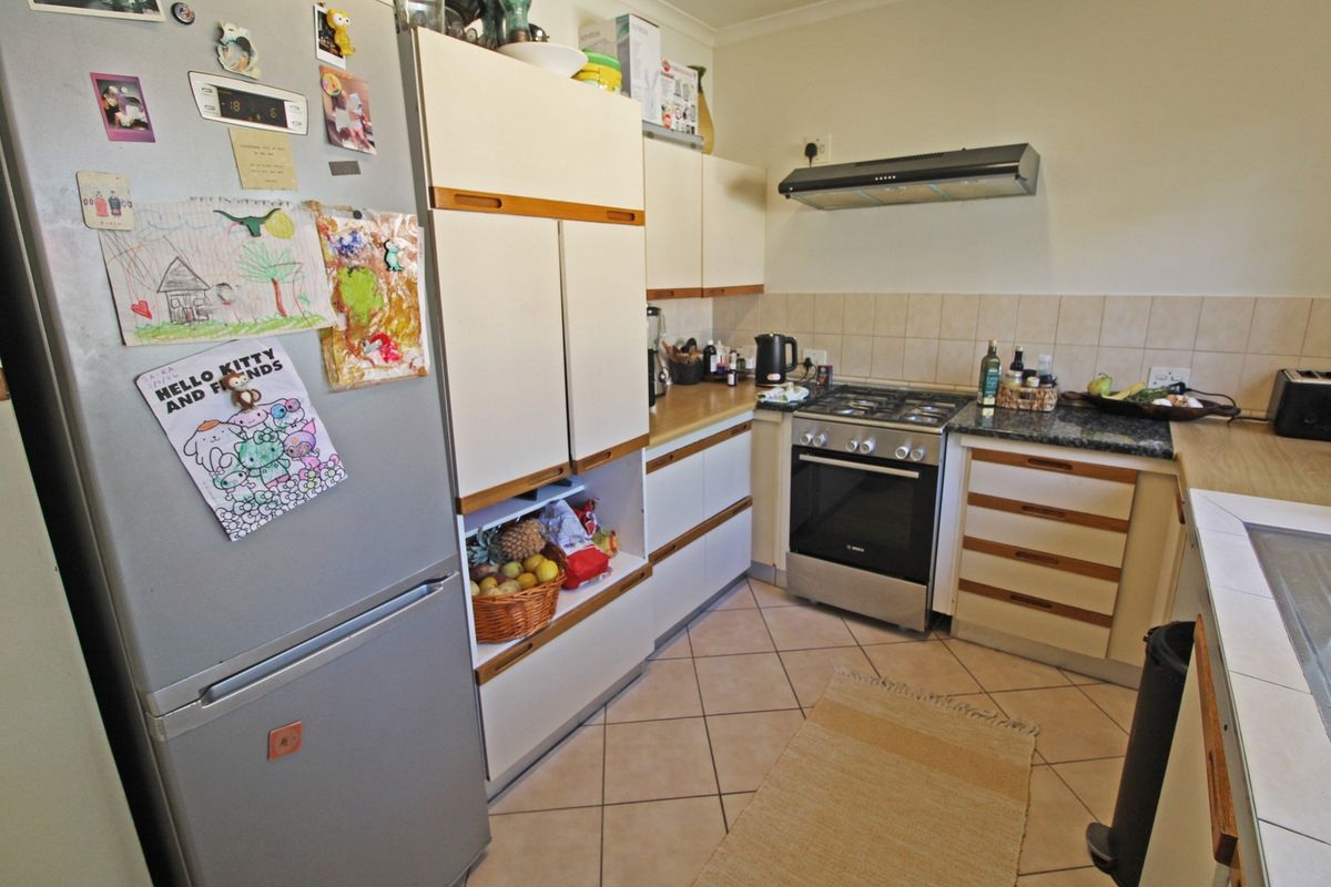 A functional kitchen featuring built-in cabinetry, granite countertops, a gas hob with extractor fan, and tiled flooring.