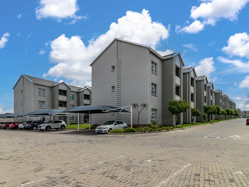 Exterior view of a modern multi-story apartment complex featuring paved parking areas and installed shade cloth carports.