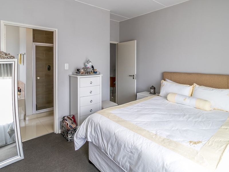 A well-maintained bedroom featuring neutral wall tones, carpeted flooring, and direct access to an en-suite bathroom with a shower enclosure.