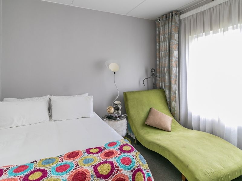 A cozy bedroom featuring neutral wall tones, carpeted flooring, and large windows dressed with curtains, providing a comfortable and functional living space.