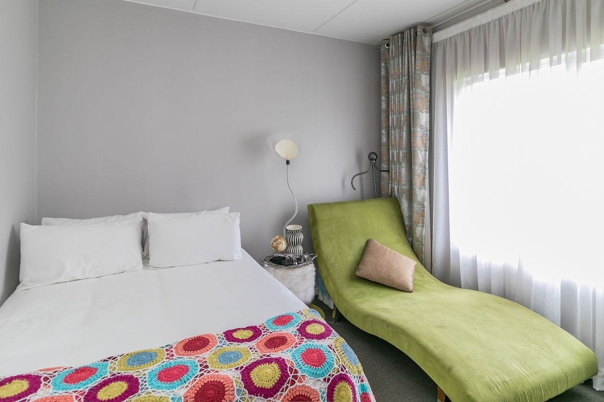 A cozy bedroom featuring neutral wall tones, carpeted flooring, and large windows dressed with curtains, providing a comfortable and functional living space.
