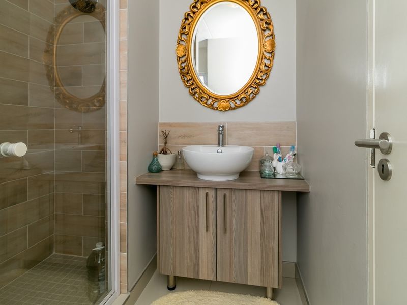 A compact bathroom featuring a modern vessel sink on a wood-finish vanity cabinet and a separate shower enclosure with neutral wall tiling.