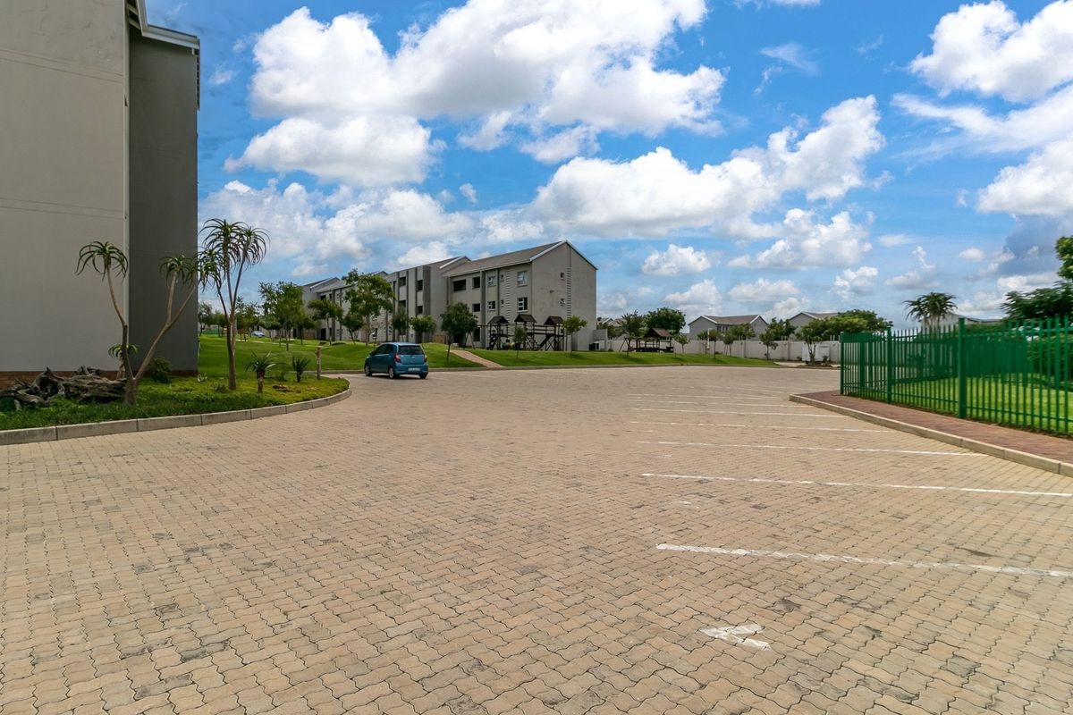 A view of the paved parking area and communal grounds within the apartment complex, featuring well-maintained landscaping and secure perimeter fencing.