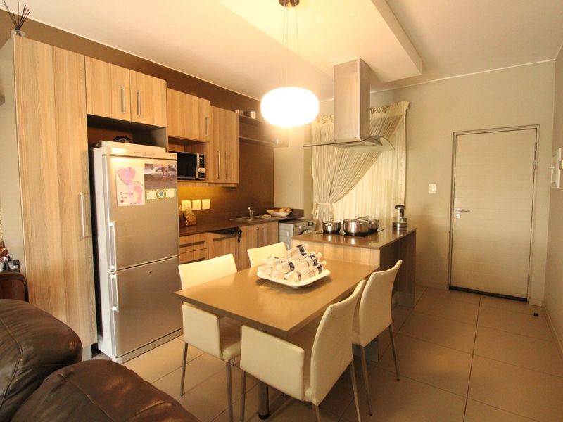 Open plan kitchen and dining area featuring modern wood-finish cabinetry, tiled flooring, and a central island with an integrated extractor fan.