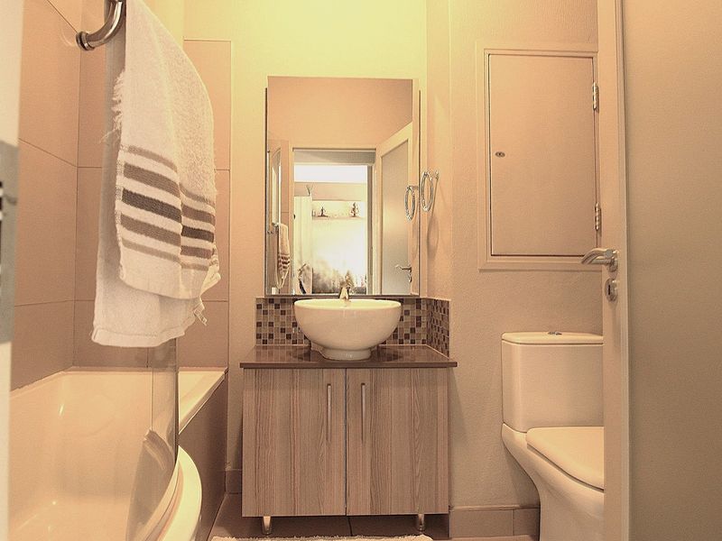 A compact bathroom featuring a modern vessel sink on a vanity cabinet, a bathtub with a glass screen, and a standard toilet.