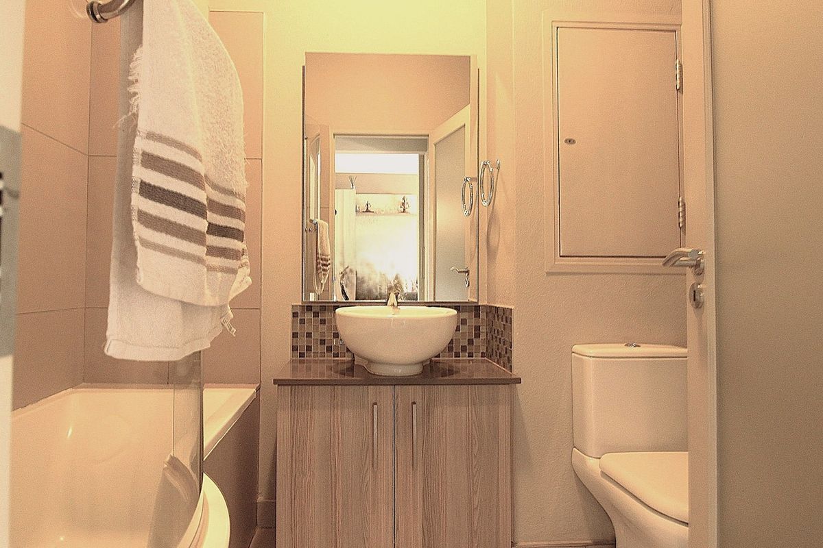 A compact bathroom featuring a modern vessel sink on a vanity cabinet, a bathtub with a glass screen, and a standard toilet.