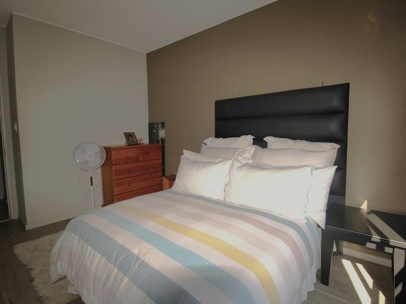 A bedroom featuring laminate flooring and a dark built-in headboard against a neutral accent wall.