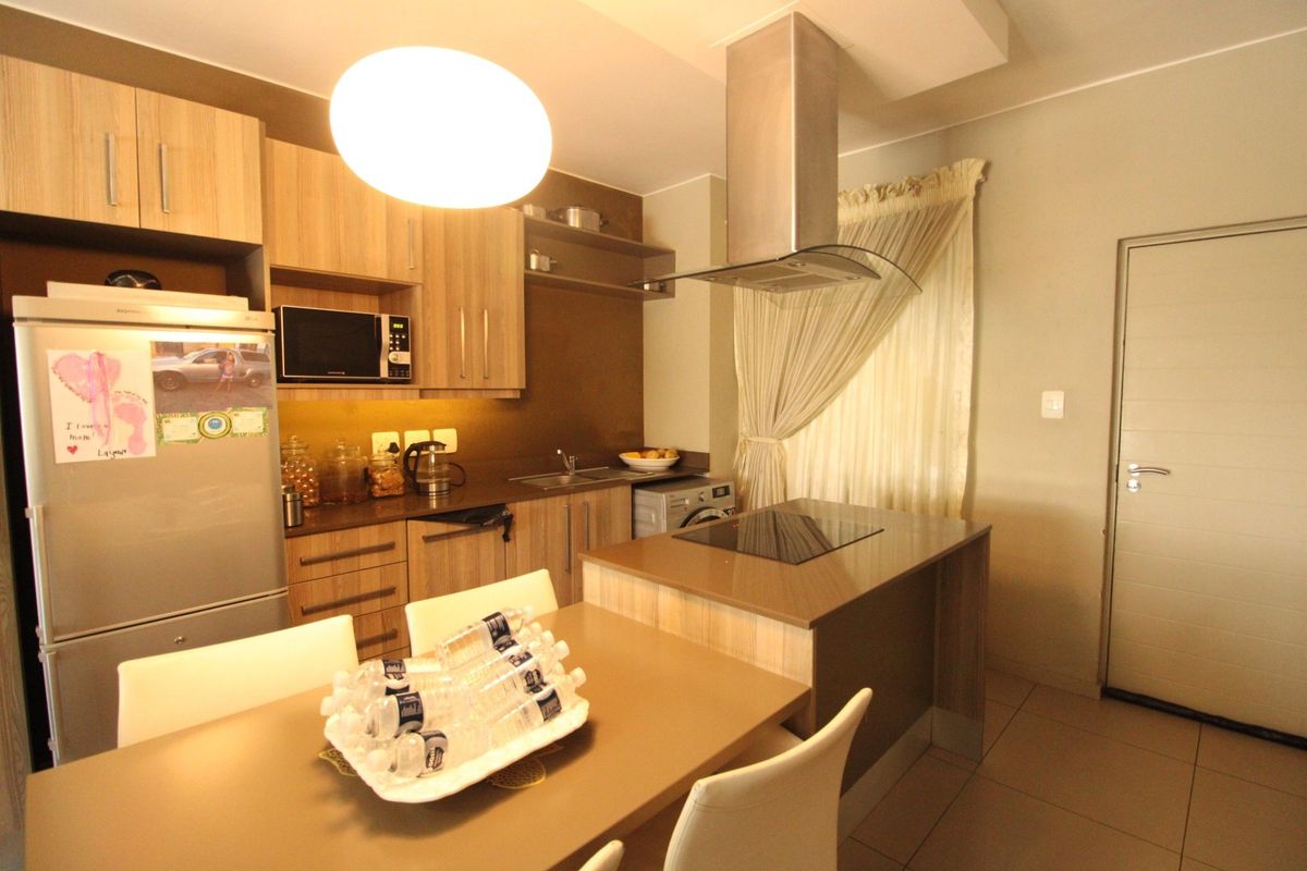 Modern kitchen featuring wood-finish cabinetry, integrated appliances, a central island with a hob, and tiled flooring.