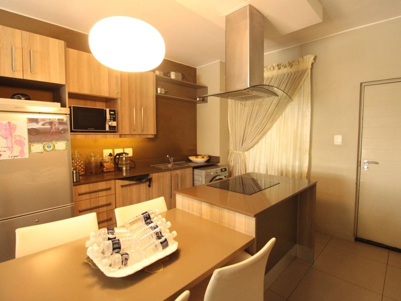 Modern kitchen featuring wood-finish cabinetry, integrated appliances, a central island with a hob, and tiled flooring.