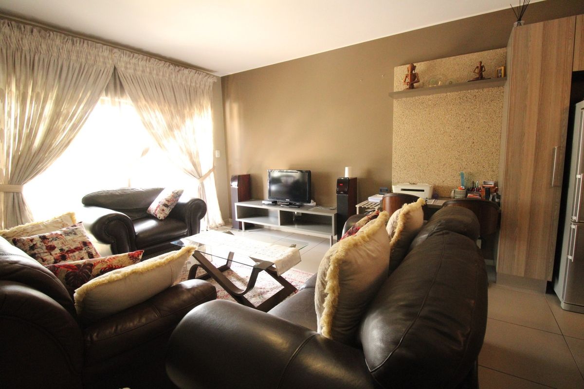 A comfortable living room featuring tiled flooring, neutral wall tones, and a built-in shelving unit, with natural light entering through a large sliding door.