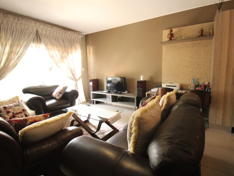 A comfortable living room featuring tiled flooring, neutral wall tones, and a built-in shelving unit, with natural light entering through a large sliding door.