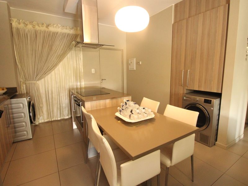 Open-plan kitchen and dining area featuring modern built-in cabinetry, integrated appliances, and neutral tiled flooring.