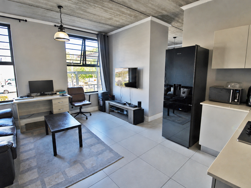 Modern open-plan living area featuring an exposed concrete ceiling, tiled floors, and a functional kitchen with built-in cabinetry and a gas hob.