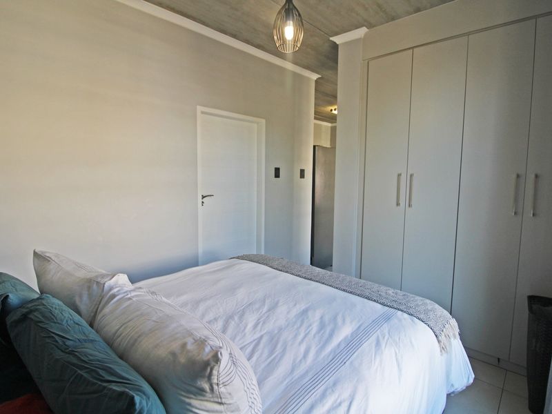A modern bedroom featuring built-in cupboards, an exposed concrete ceiling, and neutral finishes, creating a clean and contemporary living space.