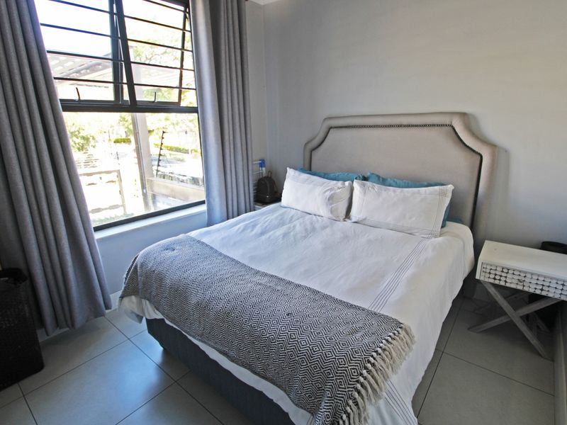 A well-lit bedroom featuring neutral tiled flooring and a large window with security bars, providing a clean and functional living space.