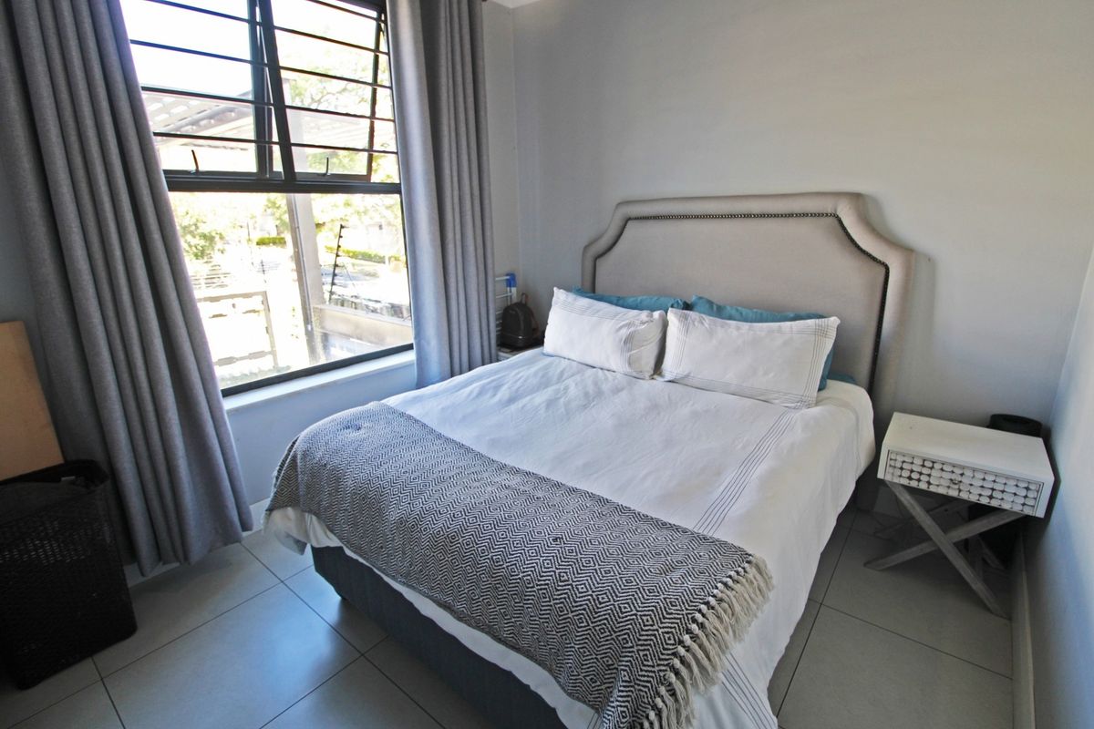 A well-lit bedroom featuring neutral tiled flooring and a large window with security bars, providing a clean and functional living space.