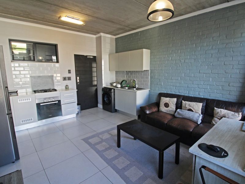 Open-plan living area featuring a modern kitchen with built-in oven, gas hob, subway tile backsplash, and an industrial-style exposed concrete ceiling.