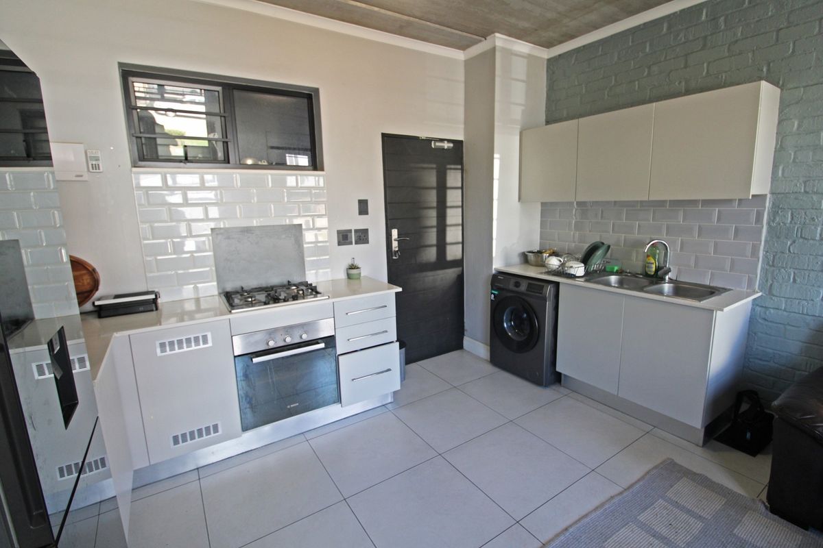 Modern kitchen featuring built-in oven, gas hob, subway tile backsplash, and sleek cabinetry, complemented by tiled flooring and an industrial-style exposed concrete ceiling.