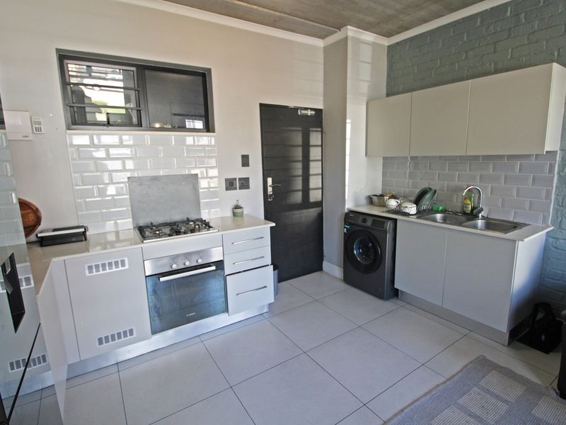 Modern kitchen featuring built-in oven, gas hob, subway tile backsplash, and sleek cabinetry, complemented by tiled flooring and an industrial-style exposed concrete ceiling.