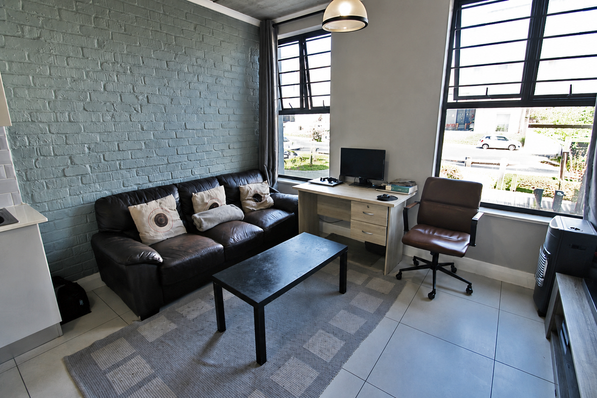 A modern living room featuring an exposed brick feature wall, large windows with black frames, and neutral tiled flooring.