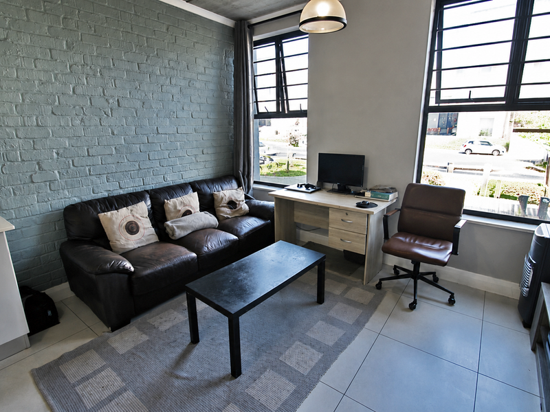 A modern living room featuring an exposed brick feature wall, large windows with black frames, and neutral tiled flooring.