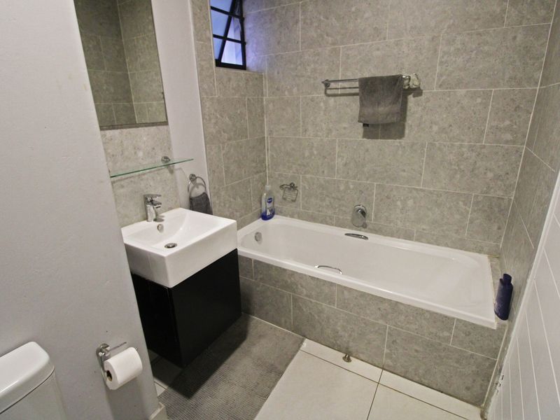 A modern bathroom featuring a built-in bathtub, a vanity cabinet with a basin, and neutral grey wall tiling.
