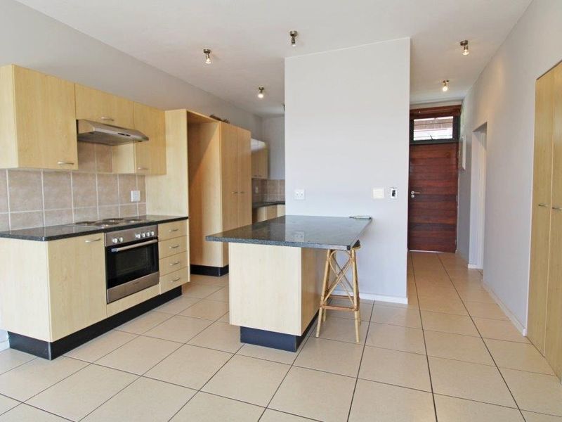 Open-plan kitchen featuring light wood cabinetry, granite countertops, built-in oven and hob, and tiled flooring, leading to an entrance hallway.