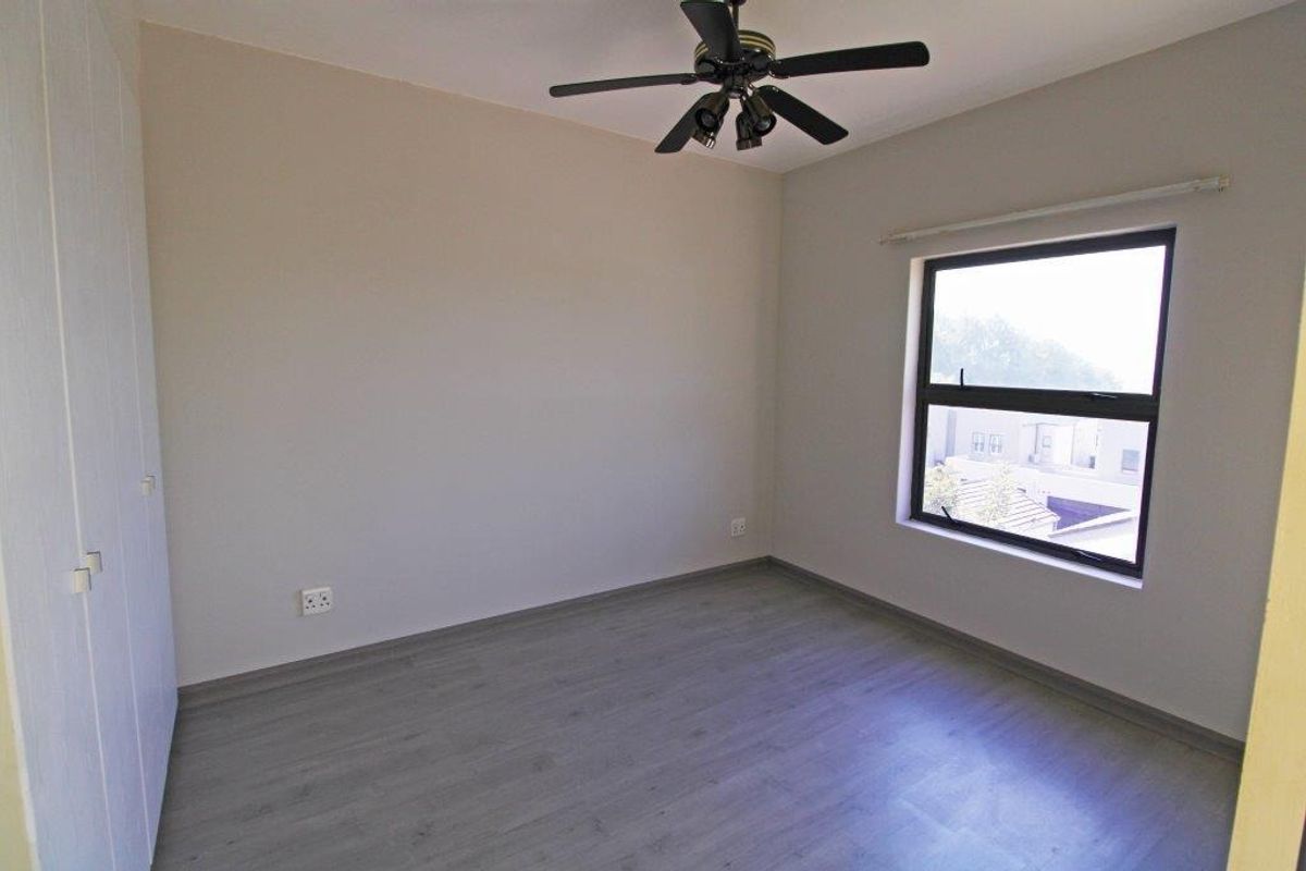 A clean, empty bedroom featuring modern laminate flooring, built-in cupboards, and a ceiling fan, offering a neutral canvas for personalization.