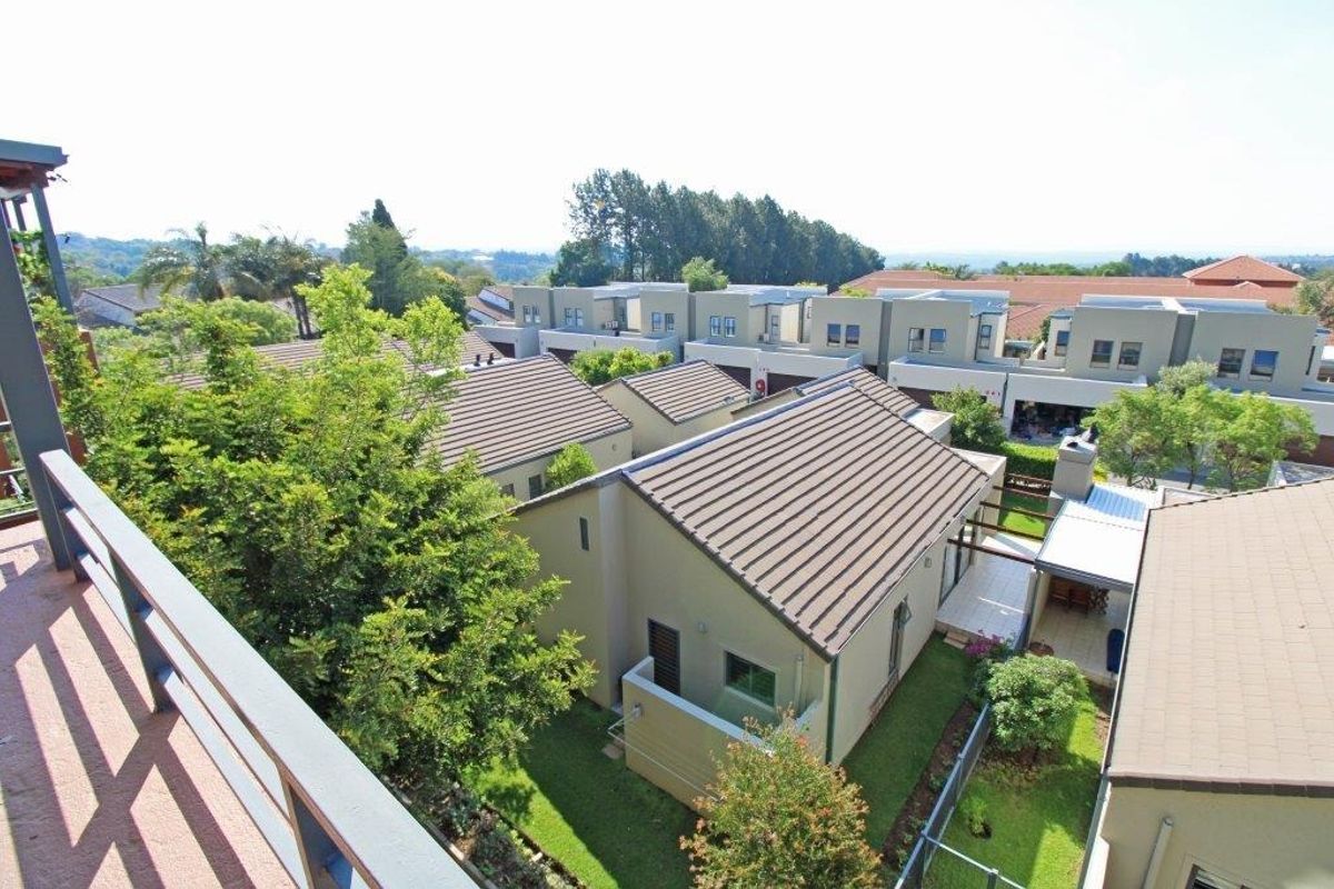 An elevated aerial view of a residential complex featuring multiple units with tiled roofs, private gardens, and paved patio areas.