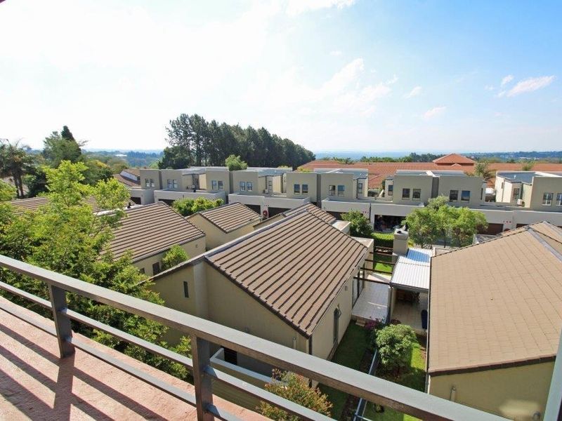 Elevated view overlooking a residential complex with tiled roofs and landscaped gardens, captured from a balcony with a metal balustrade.