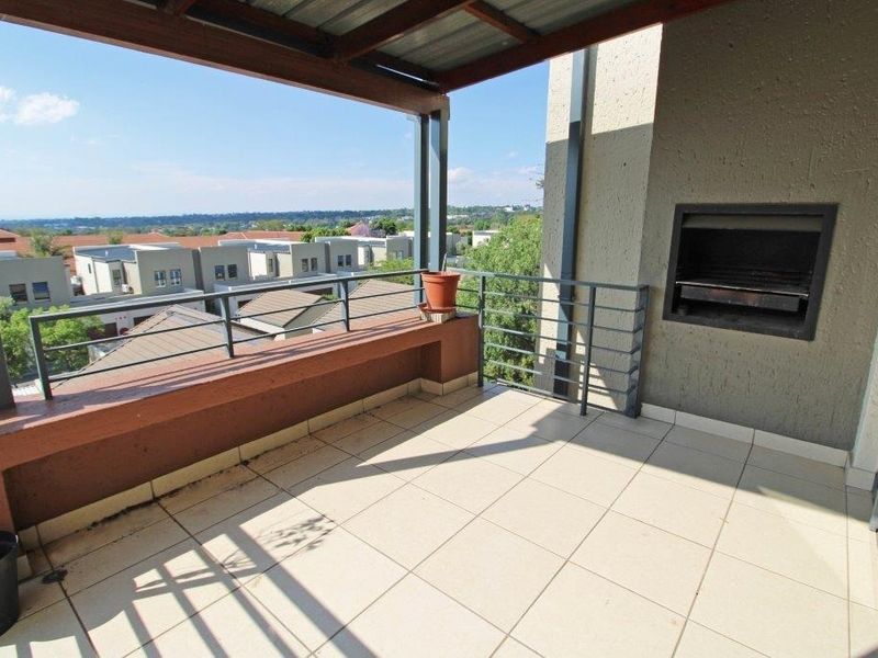 A covered balcony featuring a built-in braai, tiled flooring, and metal railings, offering an elevated view of the surrounding residential area.