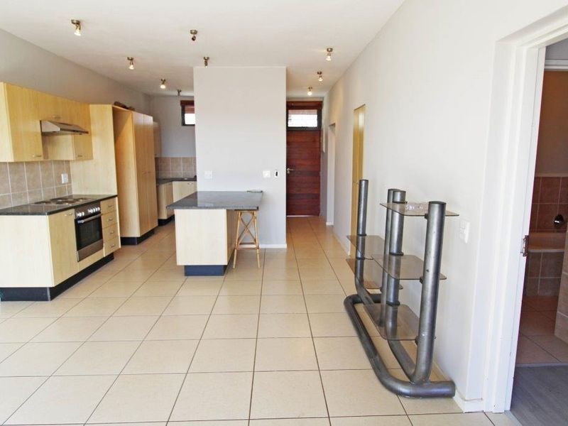Open-plan kitchen area featuring light wood cabinetry, granite countertops, built-in appliances, and tiled flooring, leading to an entrance hallway.