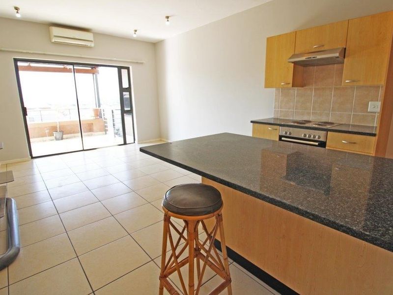 Open-plan living area featuring a kitchen with granite countertops, built-in appliances, tiled flooring, and sliding doors leading to an outdoor balcony.