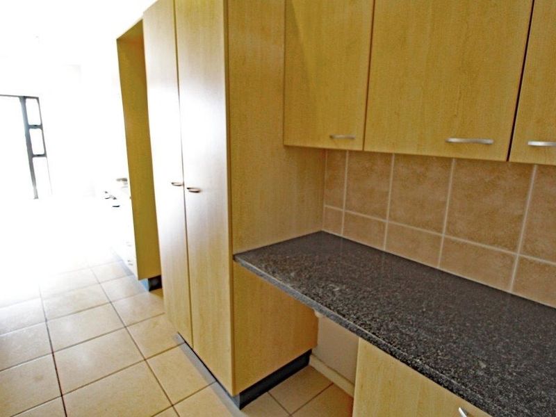 A functional kitchen area featuring light wood-tone cabinetry, dark granite countertops, and neutral ceramic floor tiling.