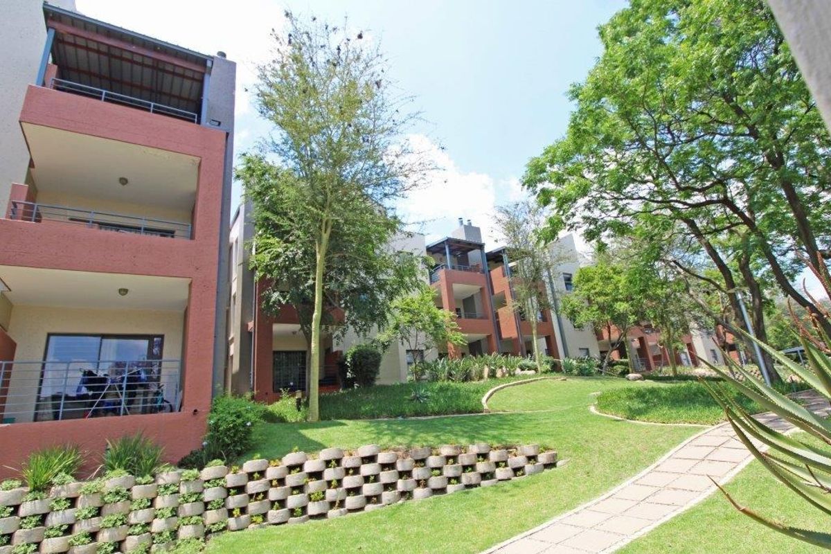 Exterior view of the apartment complex featuring multi-level balconies, a landscaped garden, and a paved walkway.