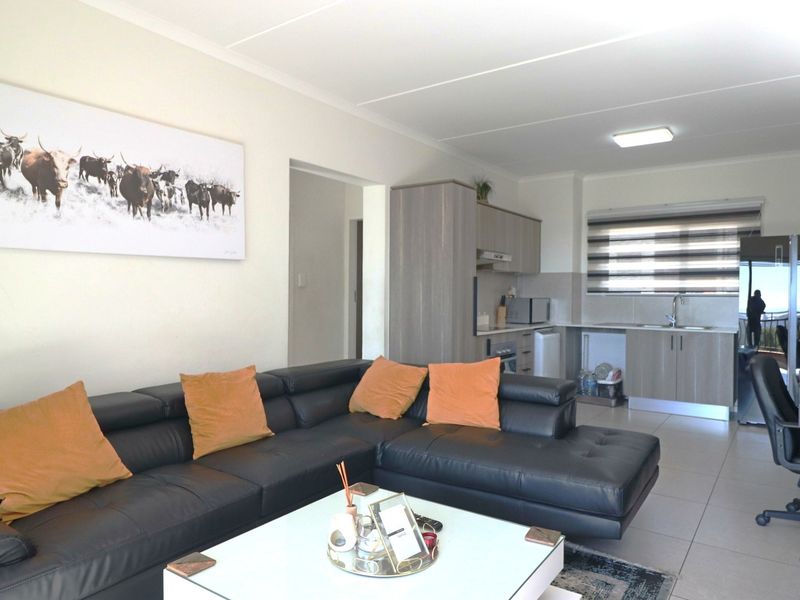 An open-plan living area featuring tiled floors and a compact kitchen with built-in cabinetry and modern finishes.