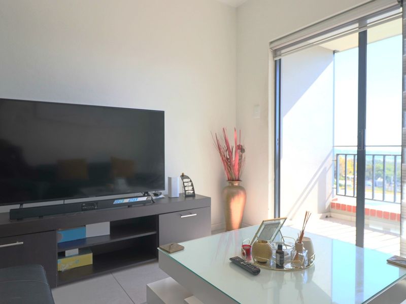 A bright living room featuring tiled flooring and a large sliding glass door that provides access to an outdoor balcony area.