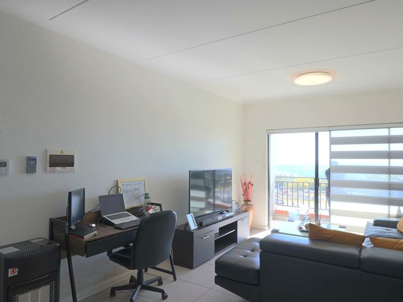A bright living room featuring tiled flooring, a ceiling light, and a sliding glass door providing access to a balcony with an outdoor view.