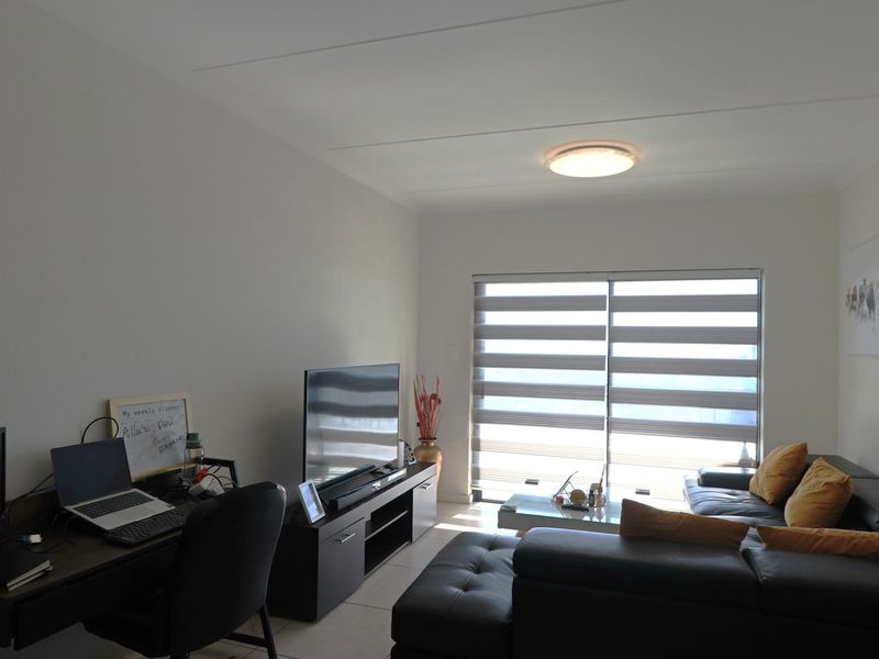 A well-lit living room featuring tiled flooring, a large sliding glass door with modern roller blinds, and a neutral interior finish.