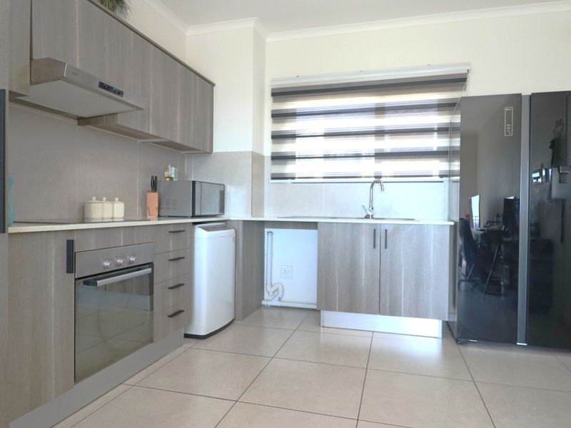 Modern kitchen featuring light wood-grain cabinetry, integrated oven and extractor fan, tiled flooring, and a functional sink area with window blinds.