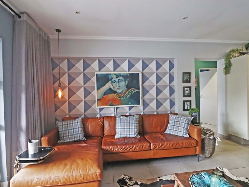 A well-lit living room featuring tiled flooring, recessed downlighting, and a decorative feature wall, creating a comfortable and modern living space.