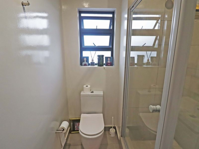 A compact bathroom featuring a modern toilet, a glass-enclosed shower, and a louver window providing natural light.