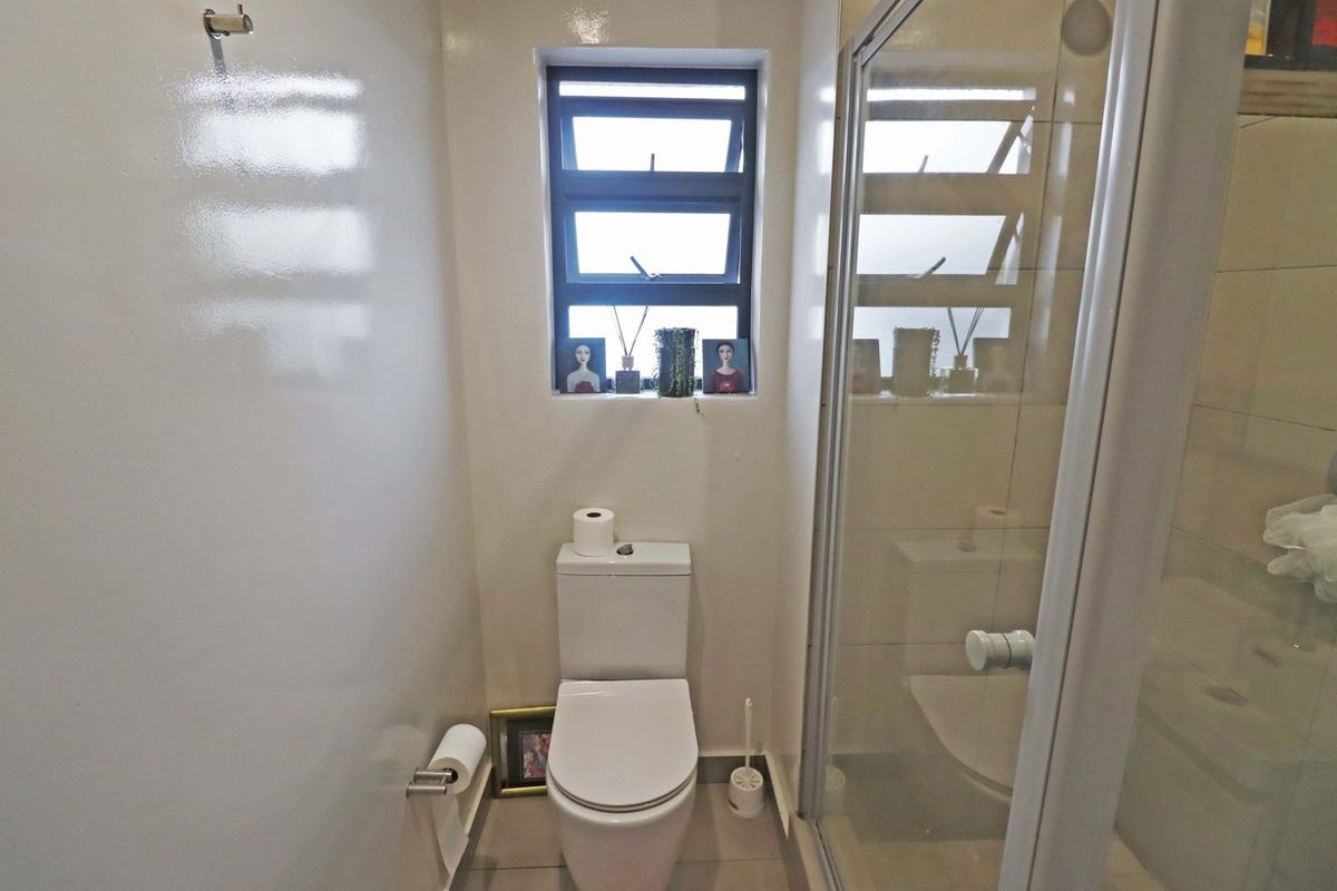 A compact bathroom featuring a modern toilet, a glass-enclosed shower, and a louver window providing natural light.