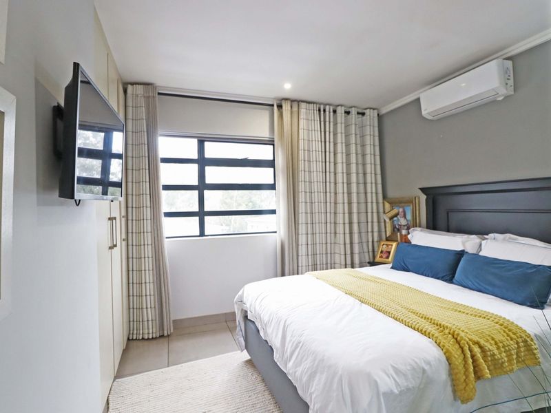 A well-maintained bedroom featuring built-in cupboards, tiled flooring, and a wall-mounted split-system air conditioner.