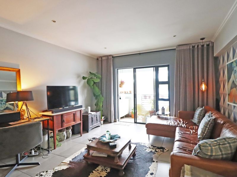 A well-lit living room featuring tiled flooring, recessed downlights, and a large sliding glass door providing access to the balcony.