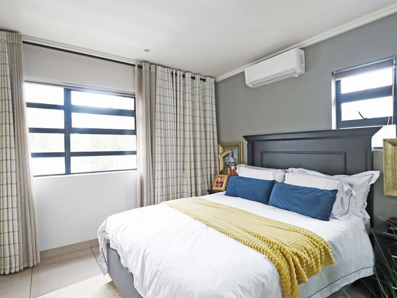 A well-maintained bedroom featuring tiled flooring, aluminium window frames, and a wall-mounted split-system air conditioner for climate control.