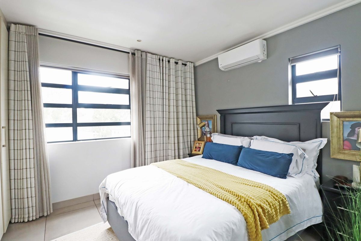 A well-maintained bedroom featuring tiled flooring, aluminium window frames, and a wall-mounted split-system air conditioner for climate control.
