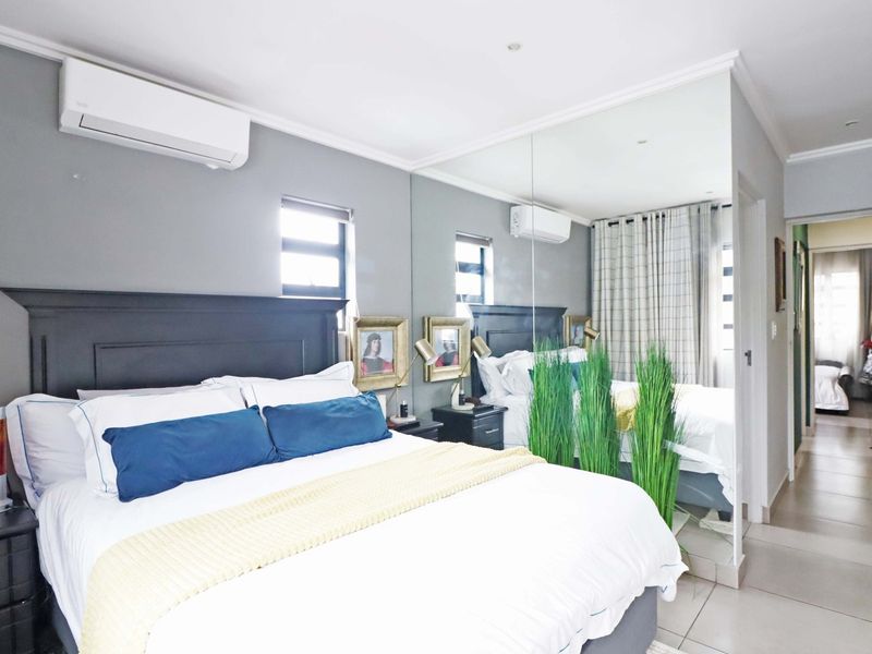 A well-maintained bedroom featuring tiled flooring, a split-system air conditioner, and a large mirrored wall that enhances the sense of space.
