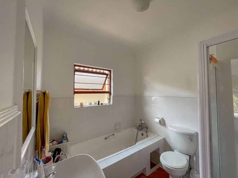 A functional bathroom featuring a bathtub, separate shower enclosure, and toilet, with white wall tiling and a small casement window.